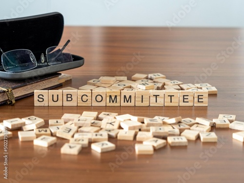 subcommittee word or concept represented by wooden letter tiles on a wooden table with glasses and a book