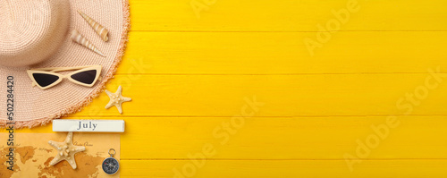 Beach accessories, map and compass on yellow wooden background with space for text