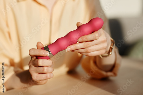 Minimal close up of young woman holding pink vibrator in hands while reviewing sex toys, copy space