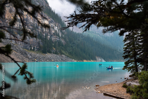 Tiny people in canoes on turquoise blue lake surrounded by mountain