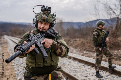 Two soldiers dogs of war mercenaries men in uniform armed service rifles aiming gun while securing the railroad in combat zone in war military battle observing territory patrolling area during mission