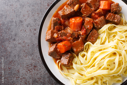 Slowly stewed spicy beef in red wine with vegetables served with noodles close-up in a plate on the table. horizontal top view from above