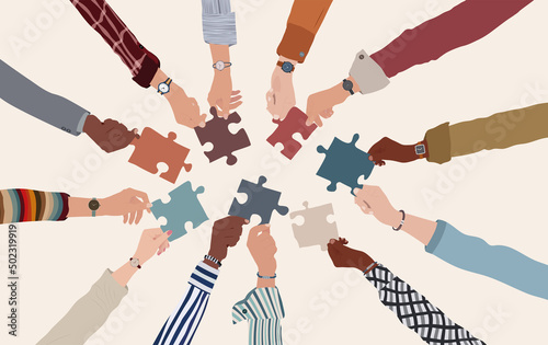 Group of multicultural business people with arms and hands in a circle holding a piece of jigsaw. Co-workers of diverse ethnic groups and cultures. Cooperate - collaborate. Teamwork