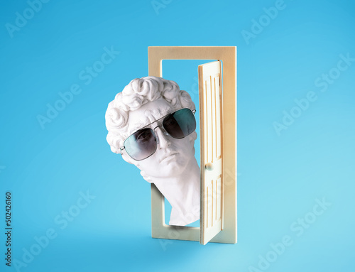 David's head in sunglasses looks out of wooden door on blue background. Summer poster.