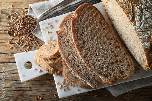 Sliced organic spelled bread on old wooden table with seeds, marble cutting board and tea towel, top view, close-up..