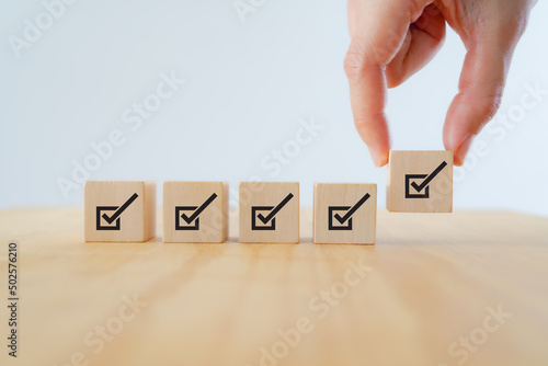 Corporate regulatory and compliance. Quality control management, ISO certification. Product, service quality warranty. Checklist survey and assessment process. Put wooden cube with check mark icon.