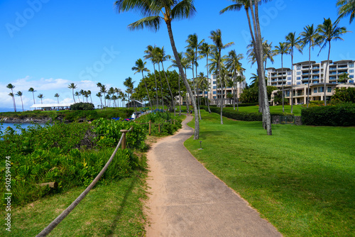 Walking path on the Kapalua Coastal Trail winding between luxury apartment buildings and the beach on Kapalua Bay in West Maui, Hawaii