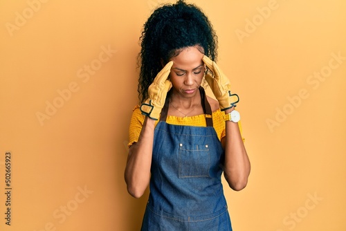 Middle age african american woman wearing professional apron with hand on head, headache because stress. suffering migraine.