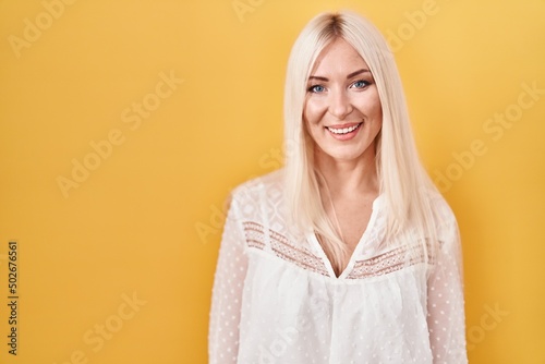 Caucasian woman standing over yellow background looking positive and happy standing and smiling with a confident smile showing teeth
