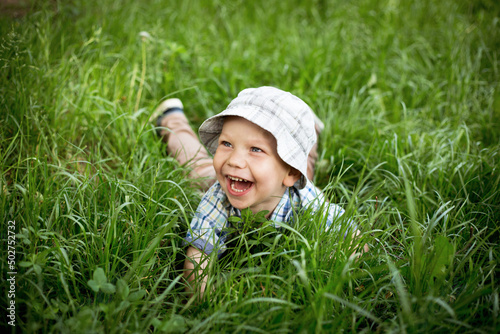 Chłopiec tarza się w trawie i śmieje w głos, dziecko turla się i leży na trawie z radością