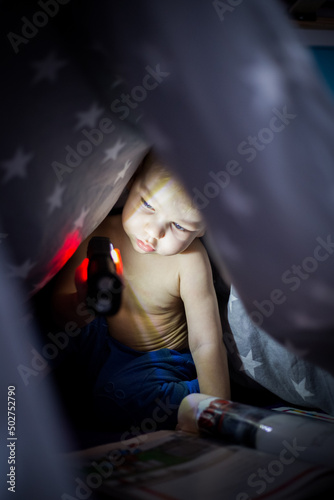 Dziecko chowa się pod kołdrą w gwiazdki i świeci sobie latarką