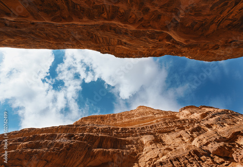 Looking up red sandstone canyon in Wadi Rum desert, blue sky with clouds above