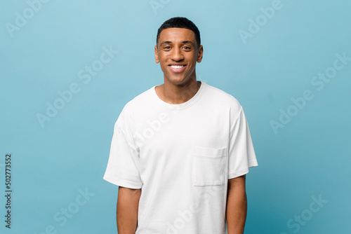 Portrait of cheerful young african-american guy wearing white casual t-shirt posing isolated on blue background. Carefree young millennial man looking at camera and laughing