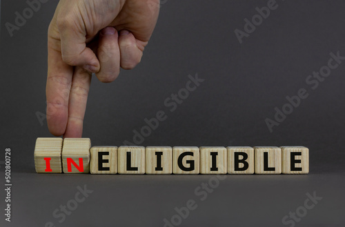 Eligible or ineligible symbol. Businessman turns wooden cubes and changes words Ineligible to Eligible. Beautiful grey table grey background. Business eligible or ineligible concept. Copy space.