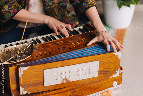 Hands of a woman sitting on the floor and playing the harmonium during the practice of kundalini yoga