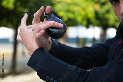 gypsy man dancing flamenco, dressed in black with castanets detail is posing with his arms up among orange trees and in the background the giralda of seville. Flamenco cultural heritage of humanity