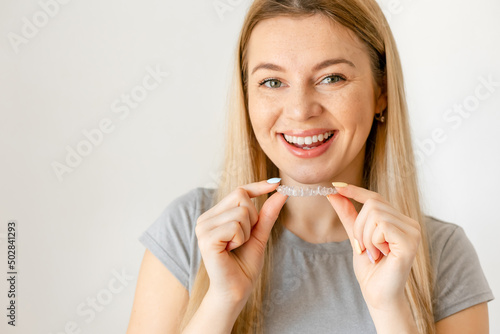 Smiling young woman over white background holding an invisible braces aligner recommending this new treatment. Dental healthcare concept.