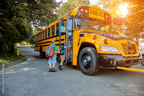 A young boy getting onto a school bus in sunshine