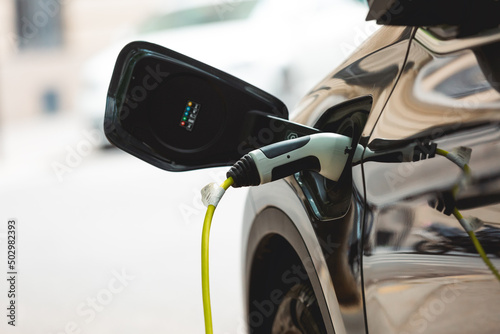 Une voiture électrique connectée à une station de recharge sur un parking. 