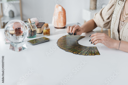 KYIV, UKRAINE - FEBRUARY 23, 2022: Cropped view of medium near tarot cards and witchcraft supplies on table.