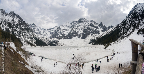 Zakopane, Poland - May 04, 2022: Panorama of Morskie oko frozen lake covered with snowy tatra mountains with people or tourists walking on snow