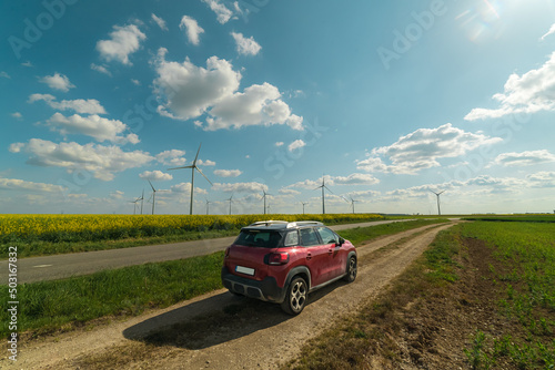 Electric car in the nature on a field, wind turbine on the background. Zero emission idea. Eco-friendly alternative energy concept. Landscape with rural road, wind power turbines. 