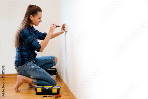 Brunette woman in plaid shirt repairs an electric socket with a screwdriver