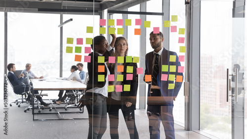 Confident African American coach teaching employees, training to use Kanban board for work on project strategy, planning tasks. Diverse business team using scrum management for teamwork