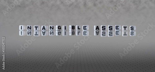 intangible assets word or concept represented by black and white letter cubes on a grey horizon background stretching to infinity