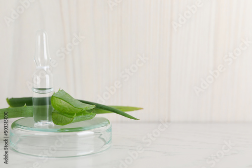 Pharmaceutical ampoule with medication and aloe leaves on white table, space for text