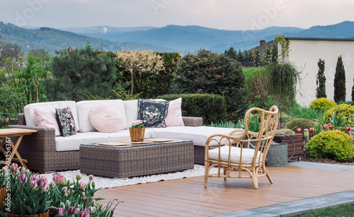 A big terrace with a comfortable leisure sofa with cushions, in a green garden during sunny vacation.