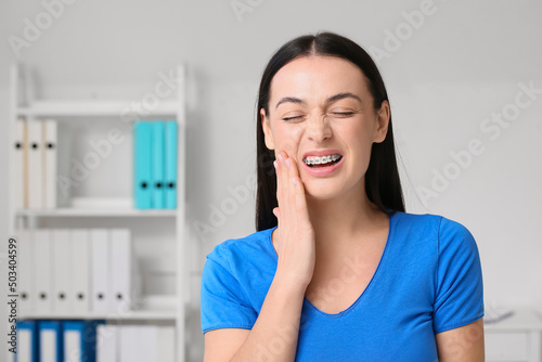 Beautiful woman with dental braces having pain in clinic