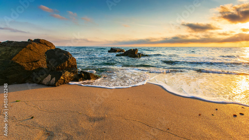 rocks on a sandy beach in morning light. beautiful seascape at sunrise. calm waves washes the shore. relaxation and summer vacation concept. gorgeous cloudscape above horizon