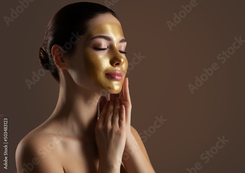 Facial peeling Golden Mask. Woman with Gold Lifting Face Mask over Dark Background. Beauty Model enjoying Skin Care Spa Cosmetology with closed Eyes. Women Anti Aging Cosmetics