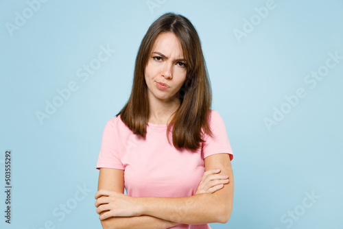 Young sad disappointed displeased caucasian woman 20s wear pink t-shirt look camera hold hands crossed folded isolated on pastel plain light blue background studio portrait. People lifestyle concept.