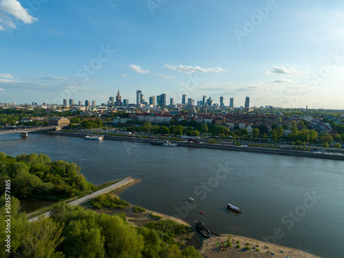 widok z lotu ptaka na centrum Warszawy, panorama miasta, wieżowce i rzekę Wisła, wiosna, zielone drzewa i niebieskie niebo