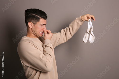 Man feeling bad smell from dirty socks on grey background