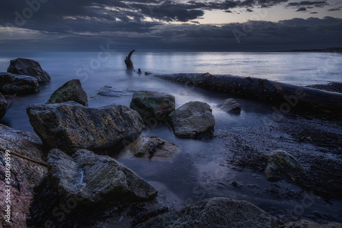 Alba o tramonto lungo la costa, con scogli e tronchi nel mare con acqua con effetto seta