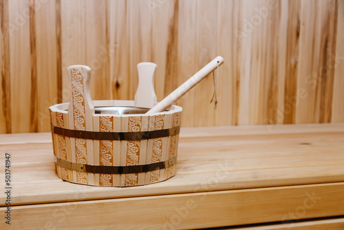 A wooden bowl of water with a carved wood pattern stands on a wooden shelf in a sauna, Russian bath, Finnish bath