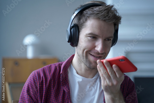 Young smiling german guy in headphones using translator app on mobile phone while studying online