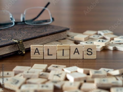alias word or concept represented by wooden letter tiles on a wooden table with glasses and a book