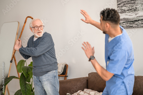 Aggressive pensioner brandishing the walking stick at his caretaker