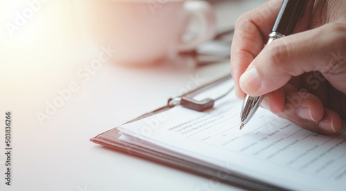 Close-up of Hand using writing pen with questionnaire or paperwork survey question filling in business company personal information form checklist document.