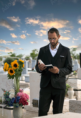 Bearded Jew in black kippah reading a Hebrew Bible, praying. Prayer in a jewish cemetery in Israel. Selective focus. Old jewish cemetery in the forest. Hasidic jew reading Torah. Vertical orientation