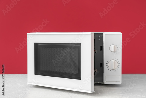 Modern microwave oven with opened door on table against color background