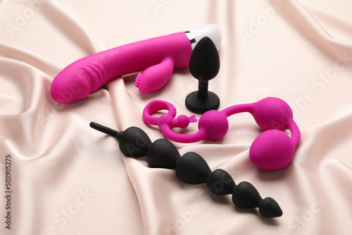 Pink and black sex toys on beige silky fabric