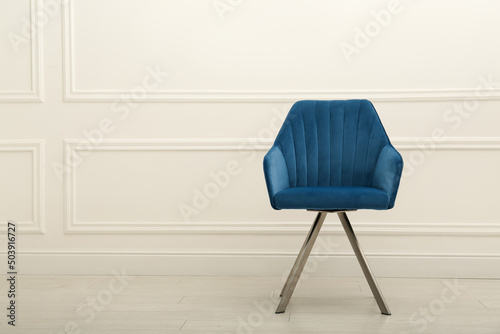 Modern blue armchair near white wall indoors. Space for text
