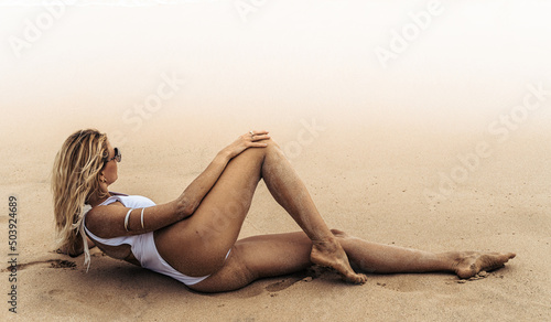Modelka w białym kostiumie kąpielowym na tropikalnej plaży na tle oceanu.
