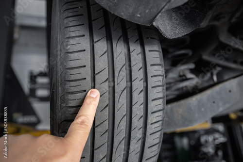 Mechanic pointing with hand at tyre wear indicator at car service center. Vehicle wheel protector control and inspection during maintenance. Tread wear check test inspection at automotive maintenance