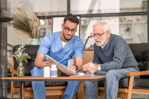 Concentrated elderly person and his caretaker perusing news